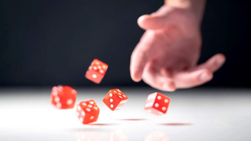 A hand tossing five red dice across a table